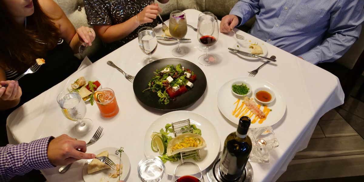 Four people sit at table filled with food and wine